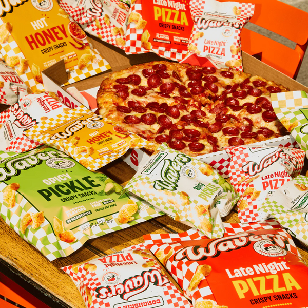 Pepperoni pizza slice surrounded by various flavored snack packages including honey, pickle, and pizza-flavored crispy snacks on wooden surface